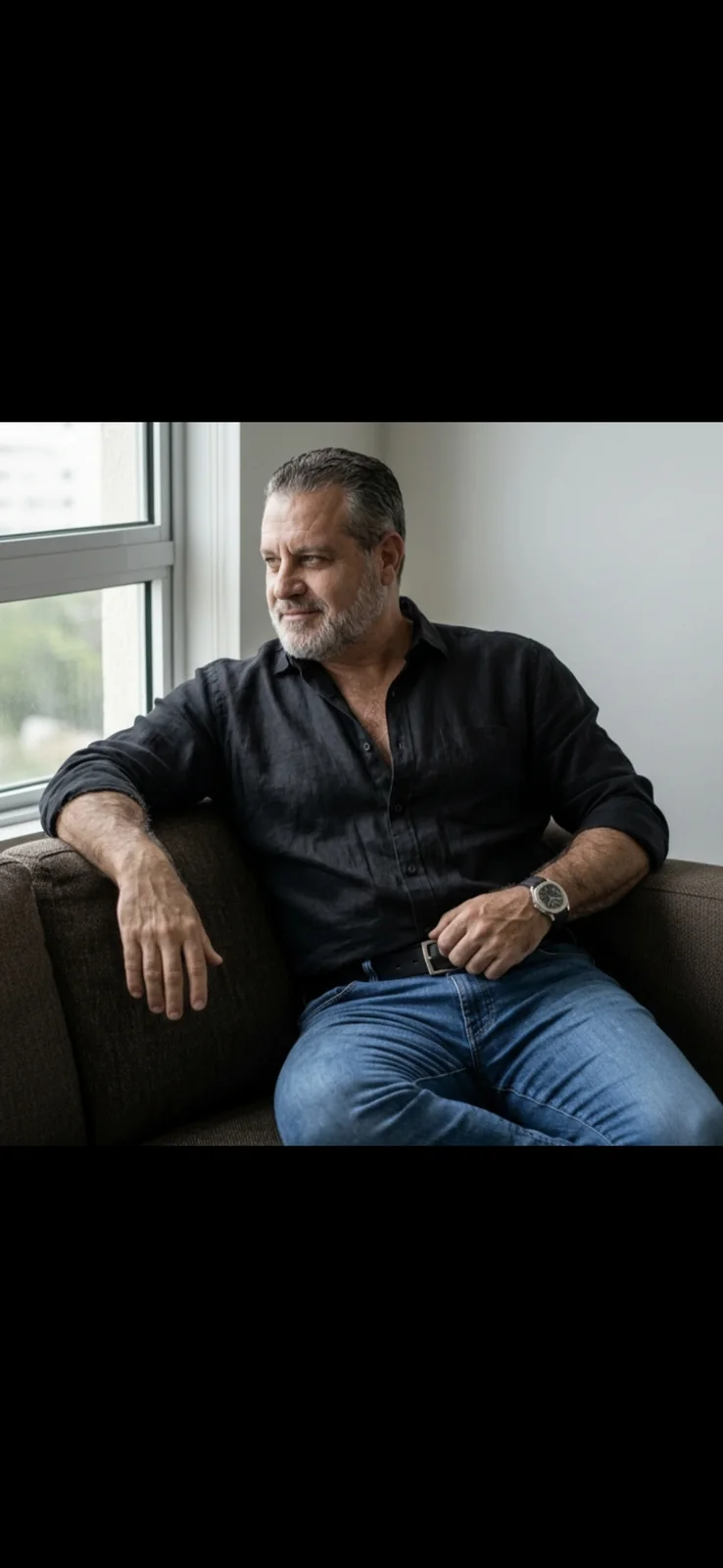 Jorge Dias sentado em um sofá, usando camisa preta e jeans